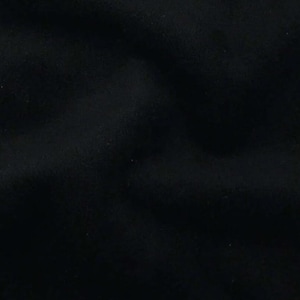 May include: A solid black fabric with a soft, matte texture. The material features subtle folds and gentle creases that create natural shadows across the surface, highlighting the deep, uniform black color and the dense, consistent weave of the textile.