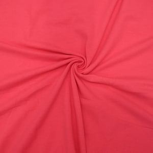 Może przedstawiać: Zbliżenie na jasnor&oacute;żowy materiał o gładkiej fakturze. Materiał jest złożony i udrapowany, co pokazuje jego miękkość i płynność.