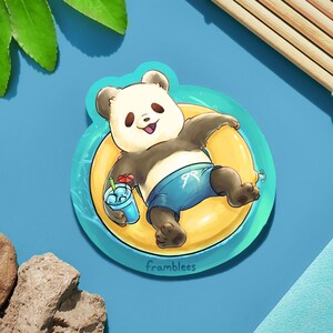May include: A sticker featuring a cartoon panda wearing a blue swimsuit and floating on a yellow inflatable ring. The panda is holding a blue drink with a red and white umbrella. The sticker has the word "framblees" printed on the bottom.