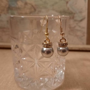 Könnte beinhalten: Ein Paar silberne Perlenohrringe mit goldfarbenen Metallfassungen und klaren Kristall-Akzenten.