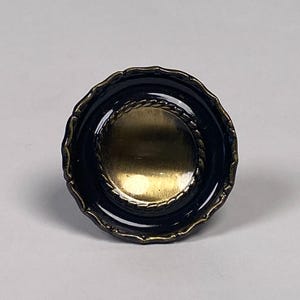 May include: A decorative cabinet knob with a dark blue, scalloped edge and a gold-colored center. A gold rope-like design encircles the center. The knob is round and appears to be made of metal.