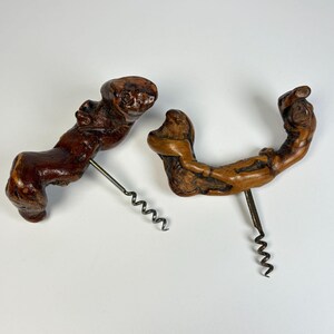 May include: Two corkscrews featuring handles crafted from raw, organic pieces of dark brown wood with natural knots and irregular shapes. Each handle is attached to a silver-toned metal spiral worm designed for removing corks from wine bottles.