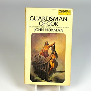 May include: A mass market paperback book titled Guardsman of Gor by John Norman, the sixteenth book of the Counter-Earth saga. The cover features a yellow background with black text and an illustration of two figures on a ship at sea.