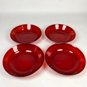 Op de afbeelding: Vier rode glazen kommen met een glanzende afwerking. De kommen zijn ovaal van vorm met een iets verhoogde rand. De kommen hebben een diepe, levendige rode kleur en het glas lijkt glad en reflecterend.