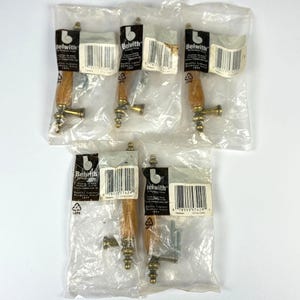 May include: Five cabinet pulls with a light brown wooden handle and brass-colored hardware are packaged in clear plastic. Each package has a label with the brand name "Belwith" and a barcode.
