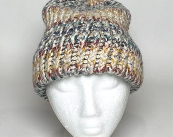 Può includere: Un berretto in maglia grossa caratterizzato da un motivo a filato variegato con macchie color crema, marrone chiaro, blu e rosso ruggine. Il cappello è realizzato con una spessa trama a coste e un bordo ripiegato, dal design multicolore.