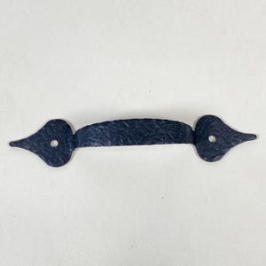 May include: A black, wrought iron handle with a textured surface. The handle has a curved centre and pointed ends, each with a single hole. This decorative hardware is suitable for cabinets, doors, or drawers.