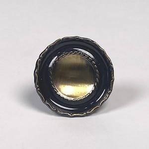 May include: A decorative cabinet knob with a dark navy blue scalloped edge and a gold-colored center. A gold rope-like design encircles the center. The knob is round and appears to be made of metal.
