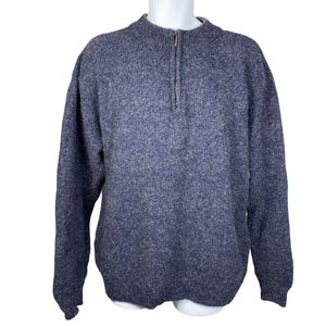 May include: A blue and gray flecked sweater with a quarter-zip closure. The sweater has a mock neck and long sleeves. The garment is displayed on a white mannequin.