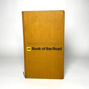 May include: A mustard yellow hardcover book titled "The Reader's Digest Book of the Road". The book features the AA logo in a yellow box. The book is standing upright. The background is white.