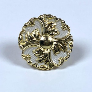May include: A decorative, round cabinet knob with a floral design. The knob features a gold-colored metal finish with white enamel accents. The center of the knob is a gold sphere. The knob is approximately 1.5 inches in diameter.
