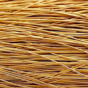 May include: Close-up of a pile of thin, gold-coloured metal wire. The wires are tightly packed and appear to be coiled or wound, creating a textured surface. The colour is a warm, metallic gold.