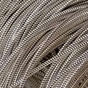May include: Close-up of a pile of silver-coloured chain. The chain is made of small, interconnected links, creating a textured surface. The links reflect light, giving the chain a shiny appearance. The chain is likely used for jewellery or craft projects.