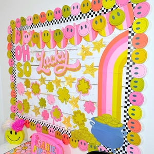 May include: A classroom bulletin board decorated with a rainbow, shamrocks, stars, and smiley faces. The board has the words "Oh So Lucky" written on it.