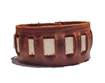 May include: A brown leather bracelet with white leather accents. The bracelet has a woven design and is adjustable.