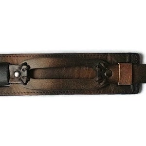 May include: A brown leather wrist cuff with a central handle and decorative metal accents. The cuff features adjustable straps with snap closures and is designed for a secure fit. The leather has a distressed finish.