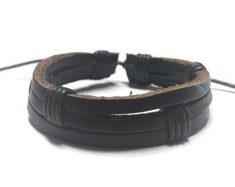 May include: A brown leather bracelet with three strands of leather woven together. The bracelet has a simple design with knots at the ends.