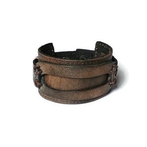 May include: A wide brown leather cuff bracelet with a distressed finish. The bracelet features multiple layers of leather and decorative stitching. The cuff is approximately 2 inches wide.