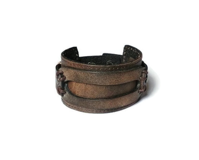 May include: A wide brown leather cuff bracelet with a distressed finish. The bracelet features multiple layers of leather and decorative stitching. The cuff is approximately 2 inches wide.
