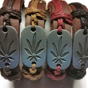 Könnte beinhalten: Vier Lederarmbänder mit einem silberfarbenen Marihuana-Blatt-Anhänger. Die Armbänder sind braun, beige, rot und schwarz.