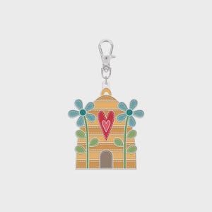 May include: A decorative keychain featuring a yellow beehive design with a red heart and two blue flowers. The keychain has a silver clasp and is made of stitched fabric.