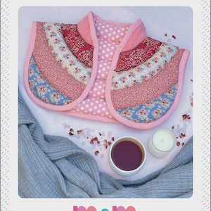 Puede incluir: Un cojín térmico ponderado para hombros y cuello con estampados rosas. La imagen presenta una taza de té, una vela y una bufanda gris. El texto de la imagen dice "WARM HUG" y "Melly and Me".