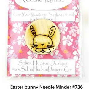 May include: Easter bunny needle minder with a wood magnet. The needle minder is a round wooden disc with a hand-drawn bunny design. The text "Keep Your Needles & Pins close at hand (made in America)" is printed on the packaging. The text "Selina Hudson Designs www.SelinaHudsonDesigns.com" is printed on the packaging. The text "Easter bunny Needle Minder #736 Wood magnet- keeps your needles close at hand UPC 638317988669" is printed below the image.