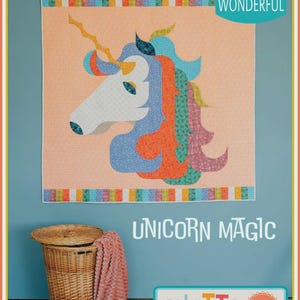 May include: A colorful quilt featuring a unicorn head with a white face, blue, orange, and green mane, and a golden horn. The quilt is displayed on a blue wall with the words "Unicorn Magic" and "Quilts" in the image.