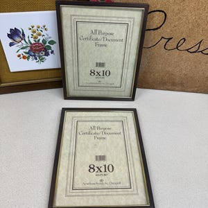 May include: Two brown 8x10 inch certificate/document frames. Each frame has a gold inner border and a printed label that reads "All Purpose Certificate/Document Frame". The frames are displayed on a white surface.
