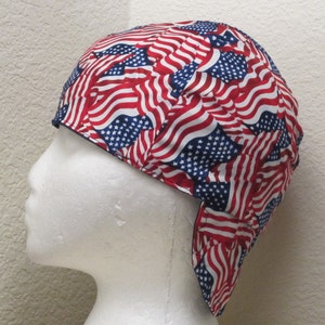 May include: A red, white, and blue welding cap with a pattern of American flags. The cap is made of a durable fabric and has a flap that can be worn down to protect the neck.