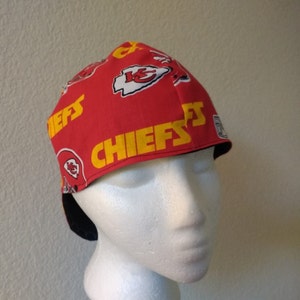 May include: Red and yellow Kansas City Chiefs themed fabric hat with a black sweatband. The hat has the words "Chiefs" printed on the front and side.