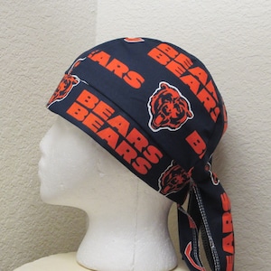 May include: A blue and orange patterned bandana with the words "Bears" and a bear logo repeated throughout. The bandana is tied around a white mannequin head.