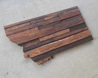 Puede incluir: Una pieza de arte de pared de madera con la forma del estado de Montana. El arte está hecho de tablones de madera recuperados en varios tonos de marrón.