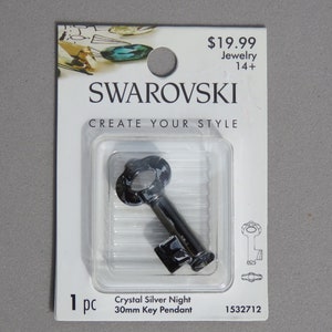 May include: A Crystal Silver Night key pendant by Swarovski, 30mm in length, displayed in a clear plastic package. The key has a decorative head and a rectangular bit. The packaging includes the Swarovski logo and the text "CREATE YOUR STYLE".