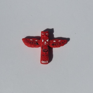 May include: Red wooden totem pole with white painted details, depicting a bird with outstretched wings.