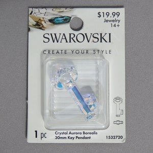 May include: A clear, iridescent crystal key pendant, 30mm in length, displayed on a white card with the Swarovski logo. The card reads "CREATE YOUR STYLE" and "Crystal Aurora Borealis".