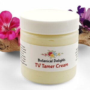 May include: A white jar with a yellow cream inside. The jar has a white label with the text "Botanical Delights TV Tamer Cream".
