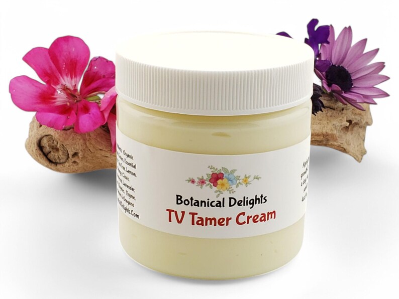 May include: A white jar with a yellow cream inside. The jar has a white label with the text "Botanical Delights TV Tamer Cream".