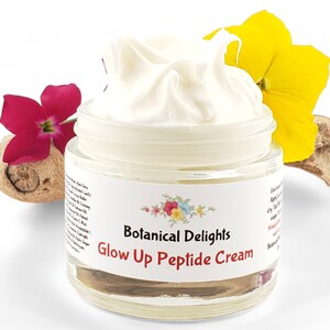 May include: A white jar of cream with a white label that says "Botanical Delights Glow Up Peptide Cream". The jar is surrounded by yellow and pink flowers.
