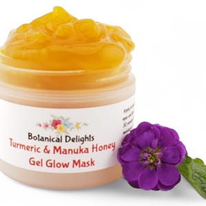 May include: A small jar of yellow turmeric and Manuka honey gel glow mask. The jar is open and the gel is visible. A purple flower with green leaves is next to the jar.
