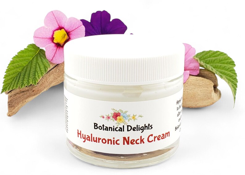 Op de afbeelding: Een witte pot met een wit deksel met Hyaluronzuur Halscr&egrave;me. De pot is gelabeld met "Botanical Delights Hyaluronic Neck Cream". De pot staat op een stuk drijfhout met roze en paarse bloemen.