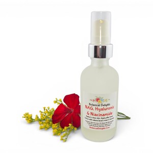 May include: A clear glass bottle with a silver pump top, labeled "NAG. Hyaluronic & Niacinamide" from Botanical Delights. A red flower and yellow sprigs are placed to the left of the bottle against a white background.