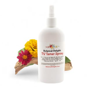 May include: A white bottle with a spray nozzle, labeled "Botanical Delights TV Tamer Spray". The bottle is sitting on a piece of driftwood with yellow and red flowers.