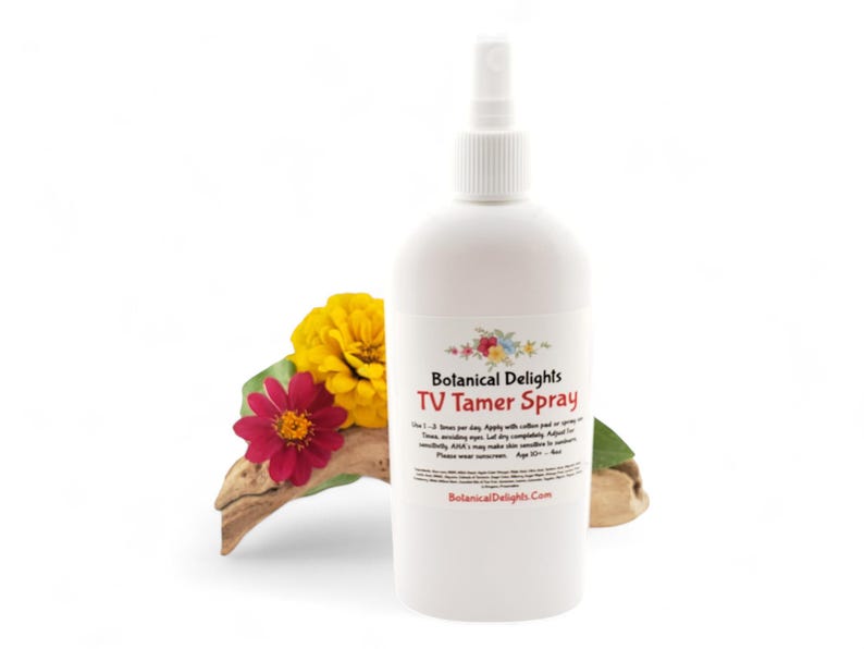 May include: A white bottle with a spray nozzle, labeled "Botanical Delights TV Tamer Spray". The bottle is sitting on a piece of driftwood with yellow and red flowers.