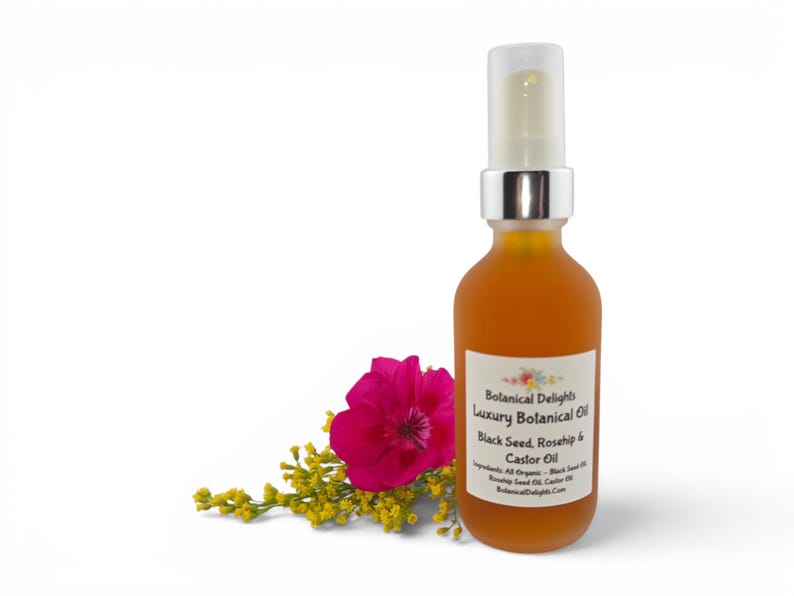 May include: A clear glass bottle with a silver pump top, filled with amber-colored liquid. The label reads "Botanical Delights Luxury Botanical Oil Black Seed, Rosehip & Castor Oil." A pink flower and yellow sprigs are next to the bottle.
