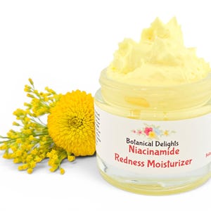 May include: A clear glass jar filled with a yellow cream, labeled "Botanical Delights Niacinamide Redness Moisturizer." A yellow flower and sprigs are next to the jar. The background is white.