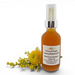 May include: A frosted amber glass bottle with a silver pump top, containing a golden liquid. The label reads "Botanical Delights Luxury Botanical Oil Black Seed, Rosehip & Castor Oil." Yellow flowers and foliage are arranged beside the bottle.