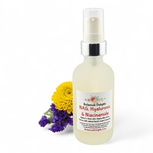 May include: A frosted glass bottle with a silver pump top, containing a skincare product. The label reads "NAG, Hyaluronic & Niacinamide." A yellow flower and purple flowers are next to the bottle. The background is white.