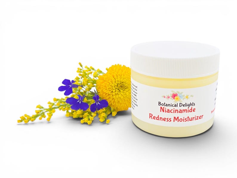 May include: A jar of Botanical Delights Niacinamide Redness Moisturizer with a white lid and a yellow label. The jar is next to a bouquet of yellow and purple flowers. The background is white.