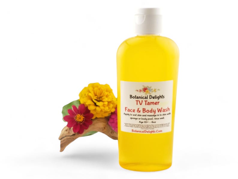 May include: A yellow bottle of Botanical Delights TV Tamer Face & Body Wash. The bottle has a white cap and a label with the product name and instructions for use. The bottle is sitting on a white background with yellow and red flowers.